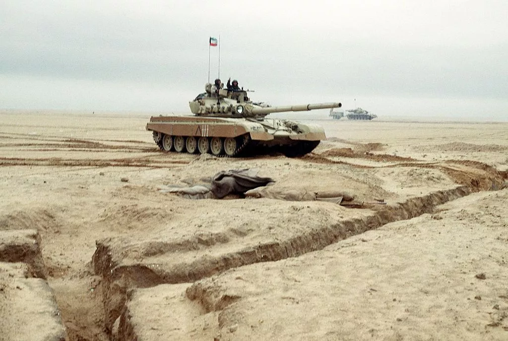 Kuwaiti flag flies from an M-84 main battle tank as a soldier gives a victory sign as the tank is driven along a channel cleared of mines during Operation Desert Storm