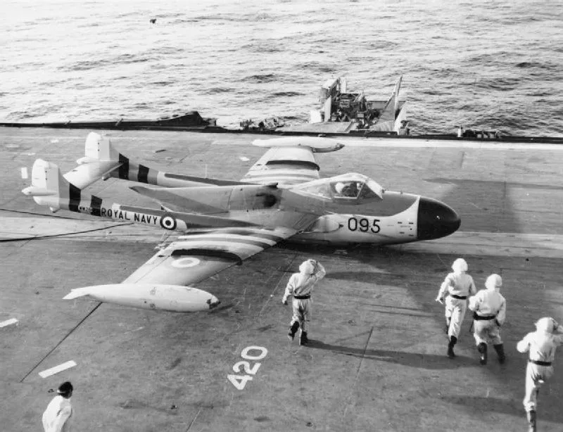 Flak damaged Sea Venom of 893 Squadron after landing on HMS EAGLE with no undercarriage. Members of the Flight Deck crew approach the aircraft after it has been brought to a standstill by the arrestor wires 4 November 1956