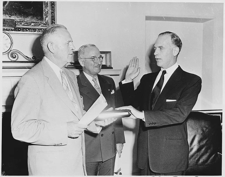 Photograph of Gordon Gray taking the oath of office as Director of the Psychological Strategy Board in the Oval Office, as President Truman looks on. 18 July 1951