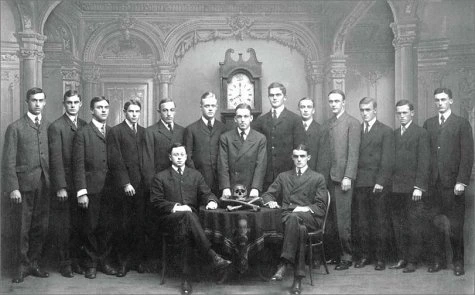 15 Bonesmen and their grandfather clock, group portrait, black and white. The Skull and Bones has a private group portrait taken for every new cohort of fifteen. It is always posed in the same manner, showing human bones and a grandfather clock at 8 p.m.