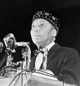 Elijah Muhammad standing behind microphones at podium / World Telegram and Sun photo by Stanley Wolfson